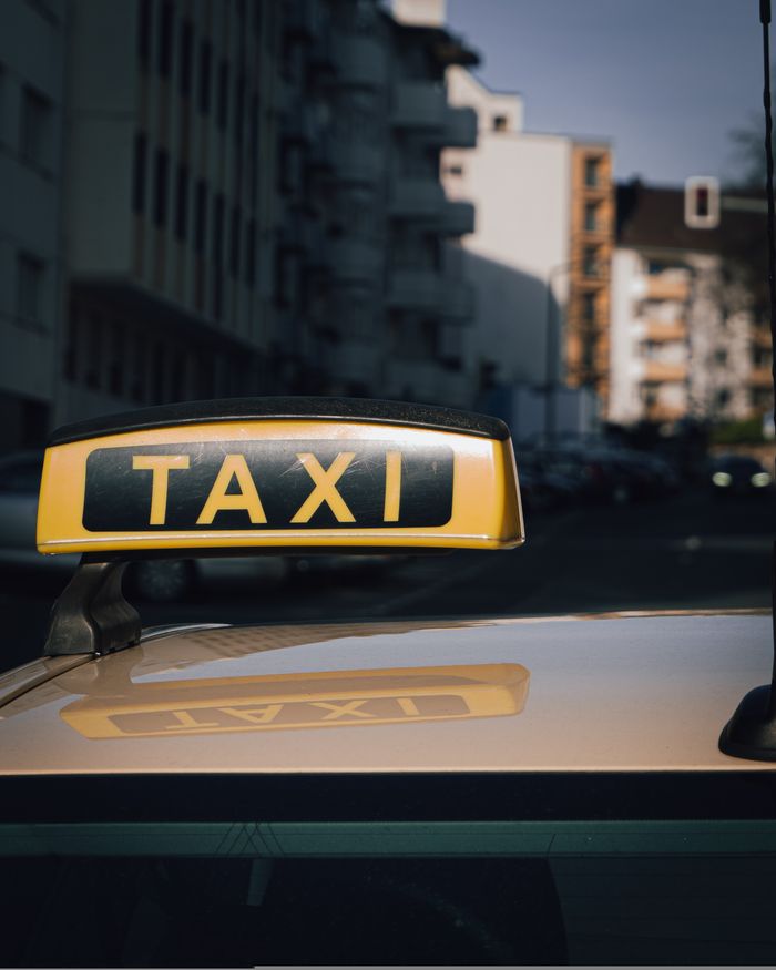 About Close-up of a taxi sign on a car roof with an urban city background.