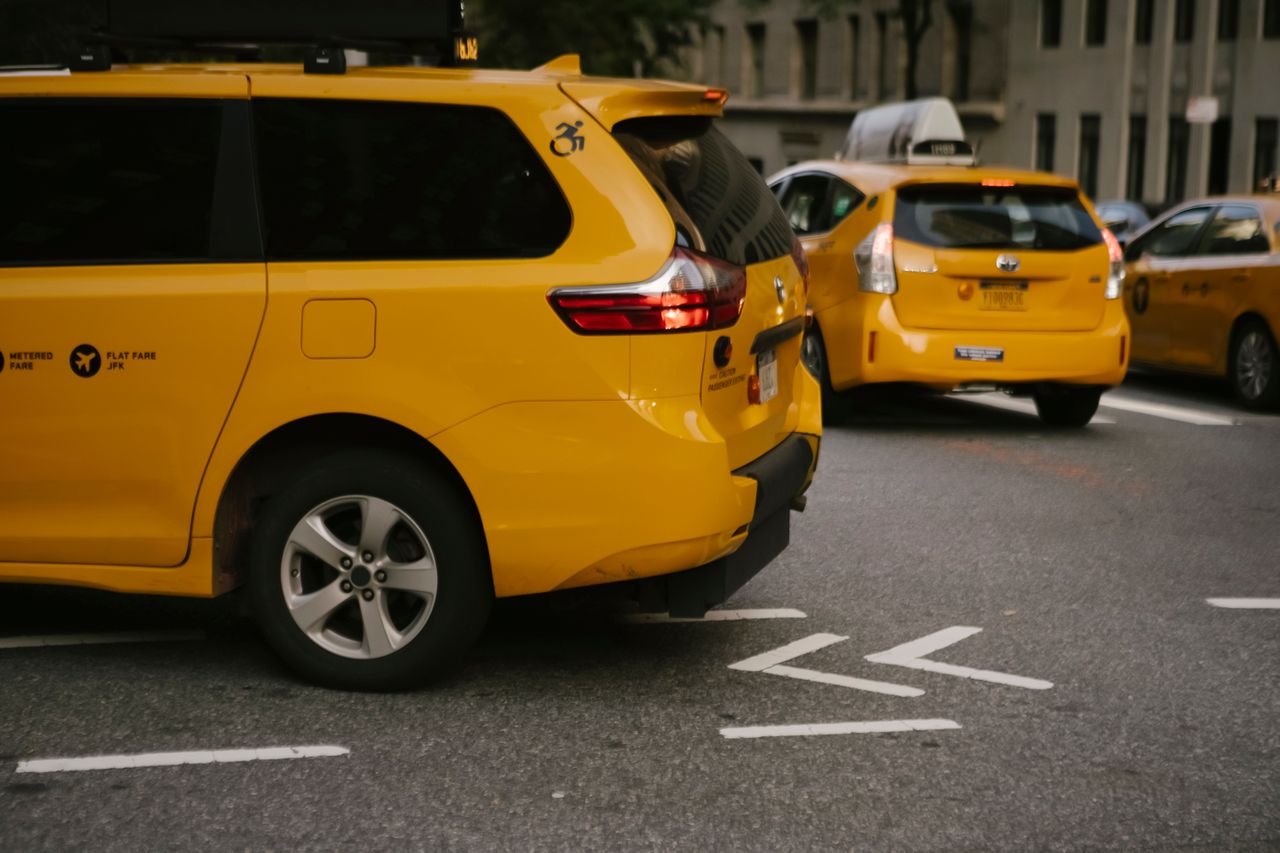 Contact Modern yellow crossover taxi cars riding on asphalt road near commercial buildings in city